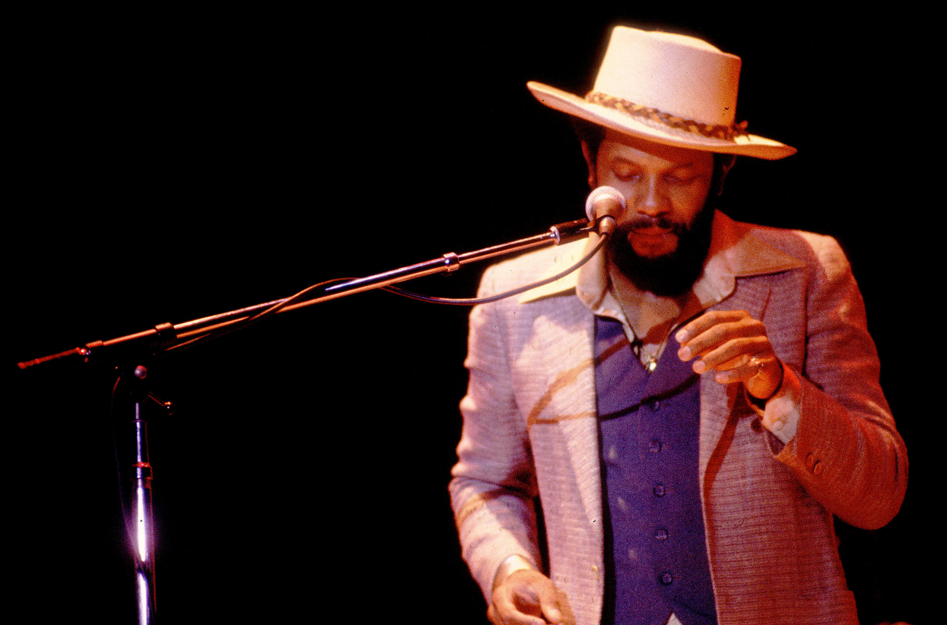 A man in a suit and hat performs on stage with a microphone.