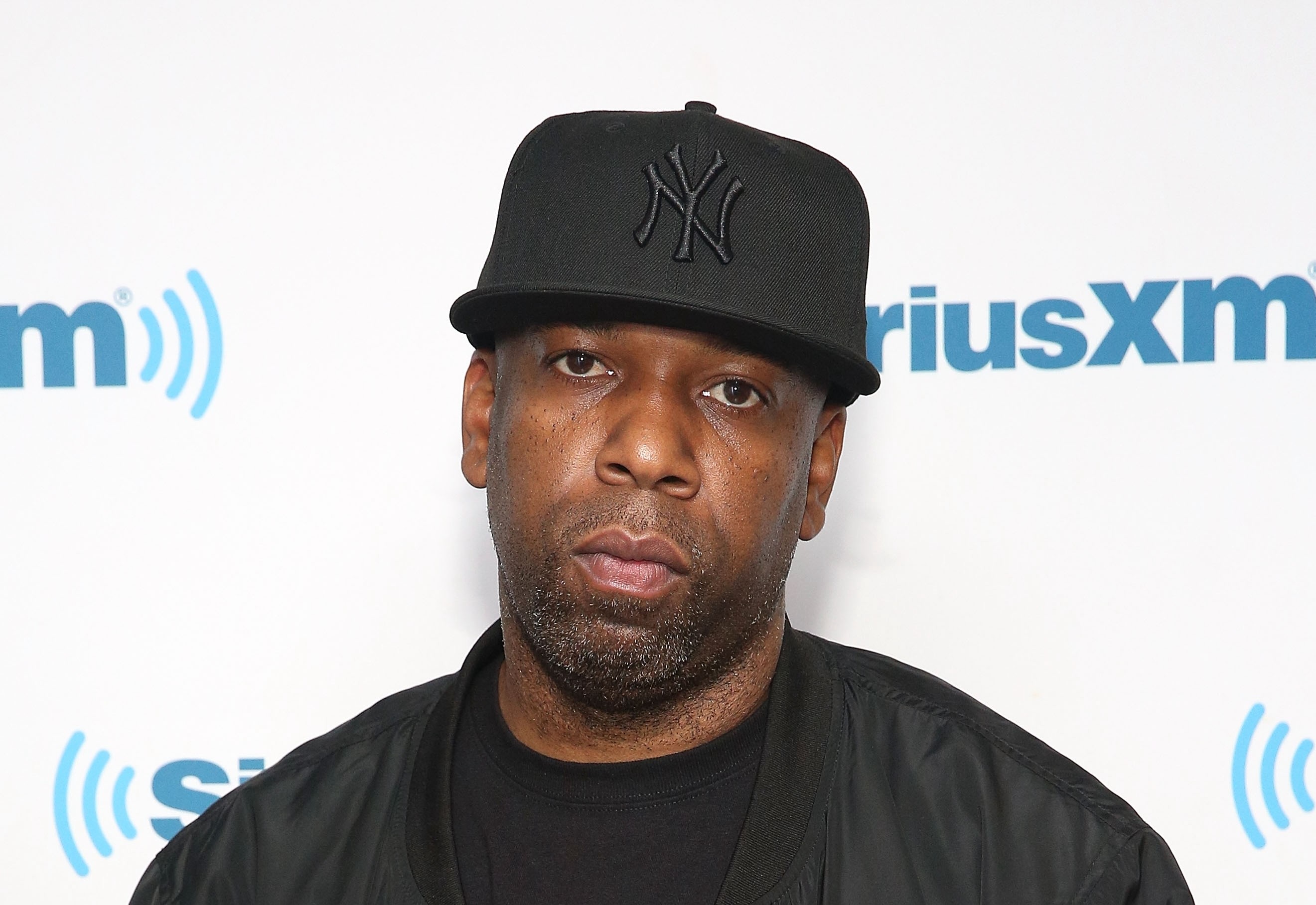A man wearing a black New York Yankees cap and black jacket stands in front of a SiriusXM backdrop.